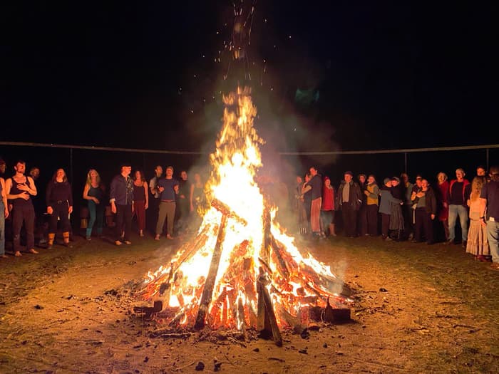 People standing in a wide circle around a bonfire at night